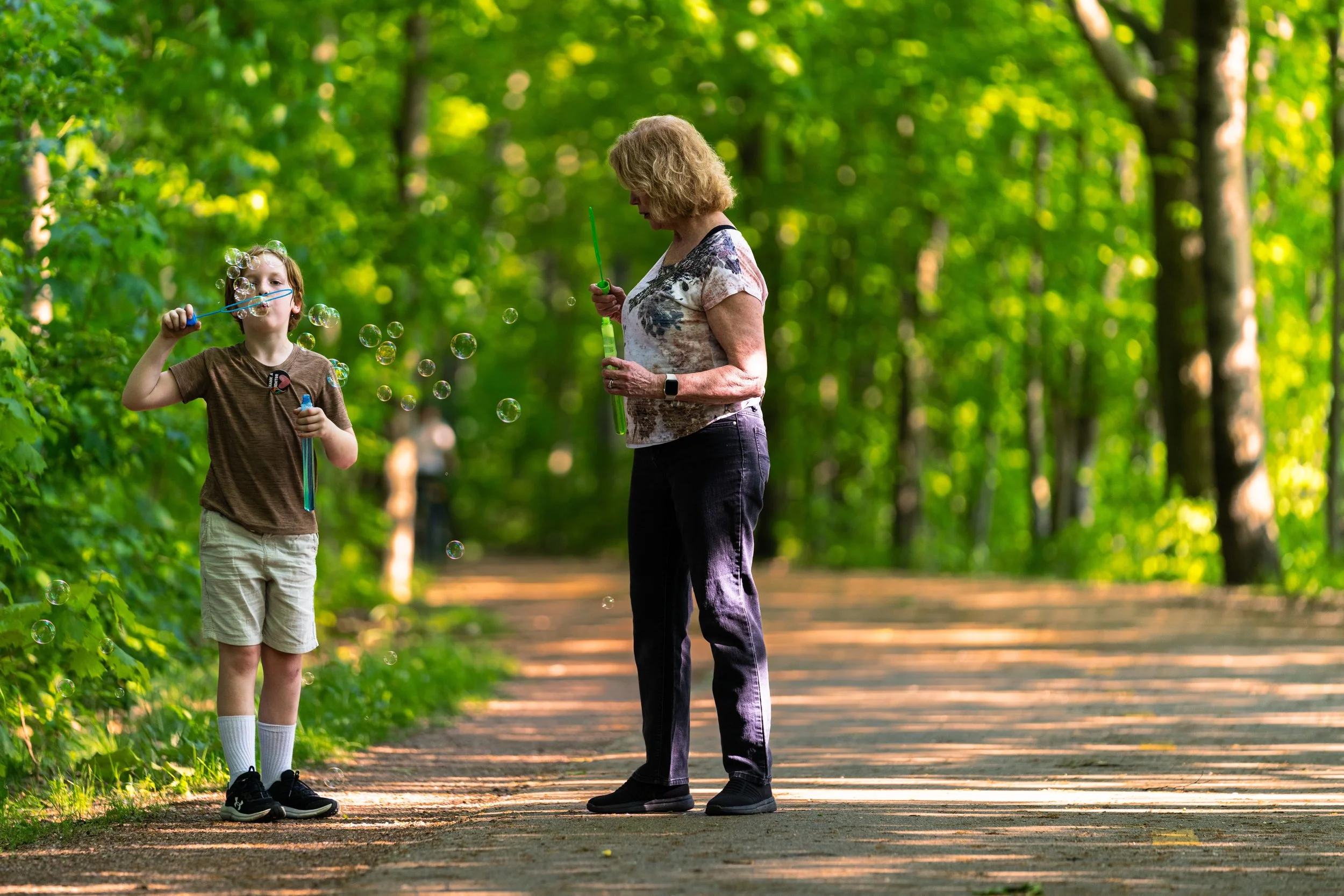 A mentor and youth blowing bubbles on a wooded trail.